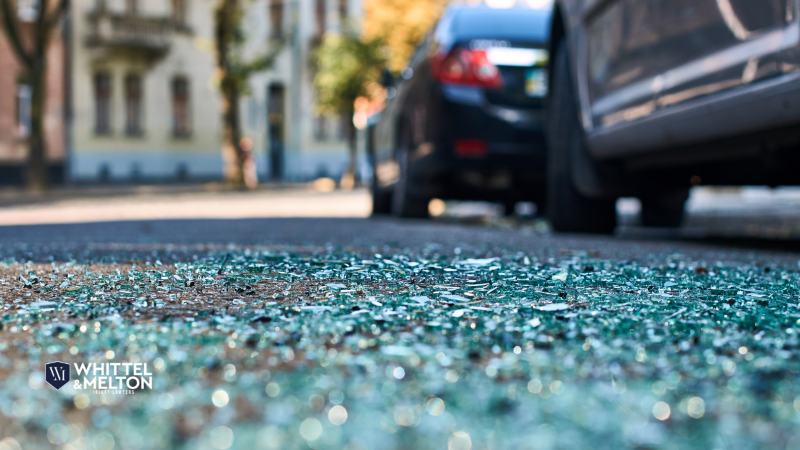 Close-up of shattered glass on the road after a car accident at a busy intersection.